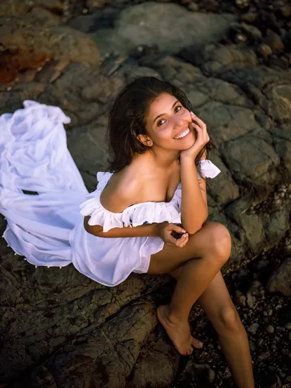 This high-angle shot offers a different perspective from the same beach series. The joyful expression and relaxed pose create a friendly and approachable vibe, while still highlighting the beautiful white dress.
