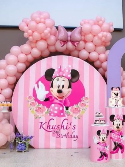 A detailed view of the Minnie Mouse birthday backdrop. The setup includes multiple pedestals for cakes and treats, all decorated to match the pink and purple theme.