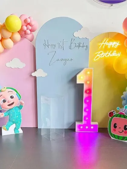 A pastel Cocomelon theme for a first birthday. This setup features colorful backdrops, a rainbow balloon arch, a marquee number '1', and character cutouts.