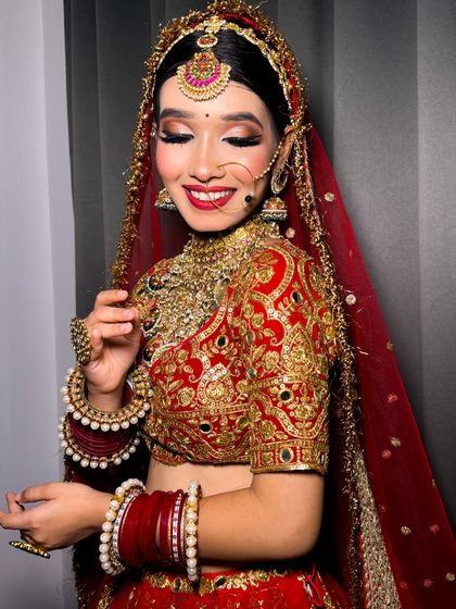 A happy, smiling bride in her red lehenga. Her makeup is glamorous and her smile is infectious.