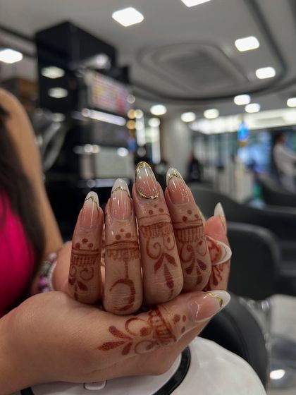 A beautiful, long almond-shaped French manicure with a delicate gold chrome line along the smile line, perfectly complementing the client's henna.