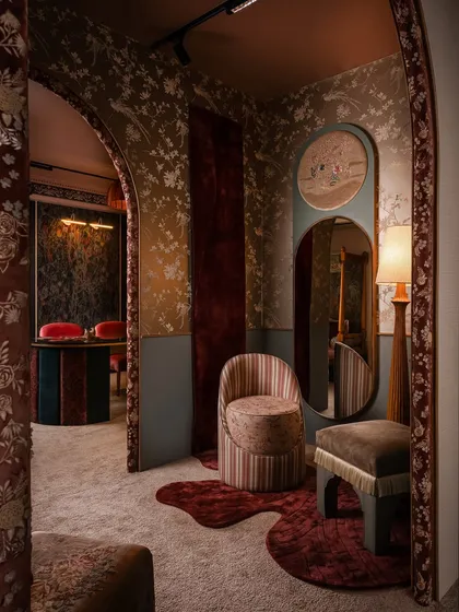 A view through the fabric-wrapped arches, showing how we layer spaces to create intriguing vignettes. The striped chair and flowing wall rug in the foreground lead the eye towards the client discussion table in the background, creating depth and interest.