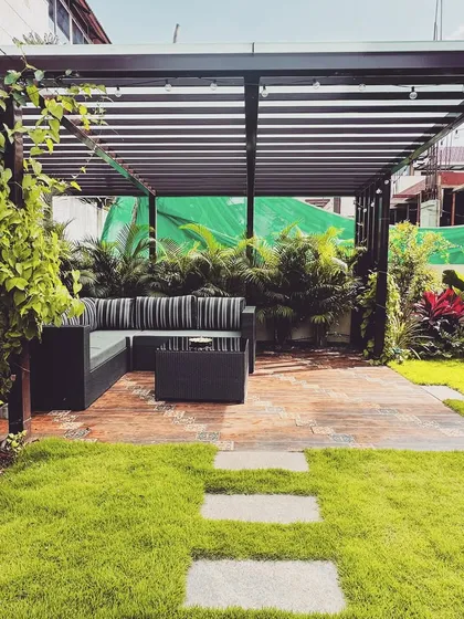 An elegant pergola creates a shaded outdoor lounge, perfect for unwinding. This structure, enveloped by climbing vines and tropical plants, provides a comfortable and stylish living area that extends the home's interior into the garden.