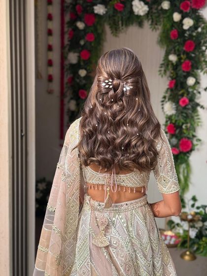 A full view of the romantic hair bow style. This hairstyle looks stunning from the back, especially with the scattered pearls catching the light against the backdrop of the client's beautiful lehenga.