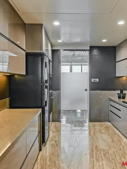 A sleek parallel kitchen with a high-gloss acrylic finish. The design incorporates handleless cabinets for a minimalist look, while the marble-finish flooring adds a touch of elegance.