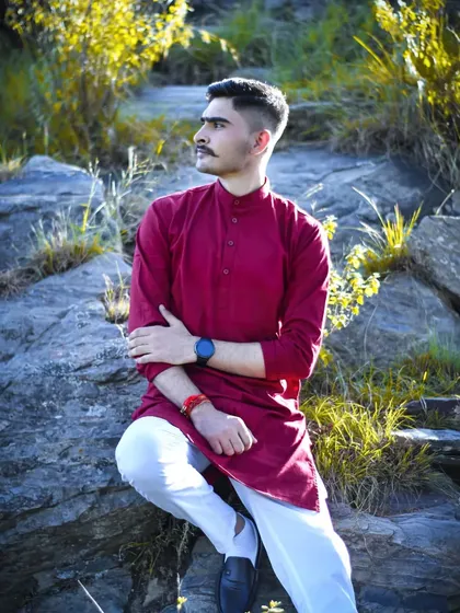 A portrait of a groom in a simple, elegant kurta, sitting in a natural, rocky landscape.