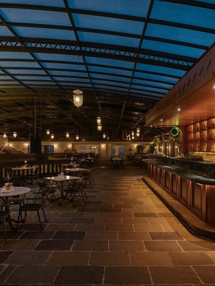 A quieter section of the bar, demonstrating how I use lighting and layout to create more intimate zones. The stone flooring and simple furnishings are contrasted with the grand architectural elements elsewhere.