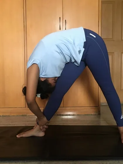 A student works on a deep hamstring stretch, Parsvottanasana, in their home space. Consistent practice like this greatly improves flexibility and can help prevent injury.