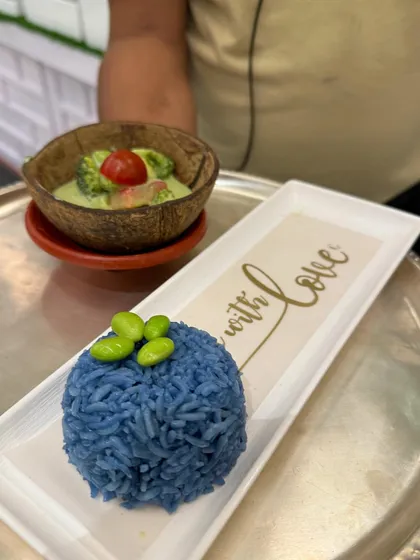 A close-up of our Thai Green Curry served with blue pea rice. The 'Made with Love' inscription on the plate reflects our philosophy of cooking from the heart.