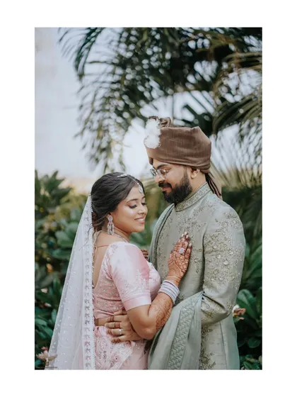 A tender moment between a couple, captured outdoors with lush palm trees in the background. The bride's gentle touch and the couple's close embrace convey a sense of comfort and deep affection.
