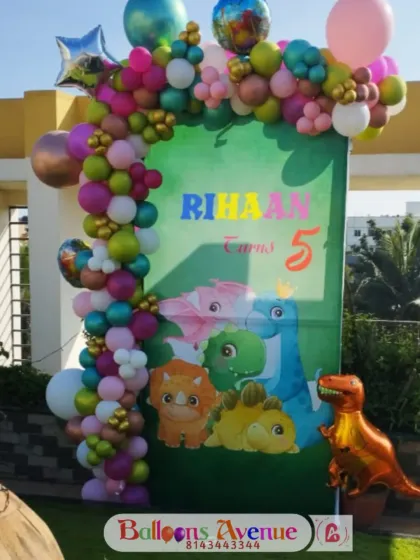 A cute dinosaur-themed entrance decoration for Rihaan's fifth birthday. The setup features a custom banner with cartoon dinosaurs and a colorful balloon arch to welcome the guests.