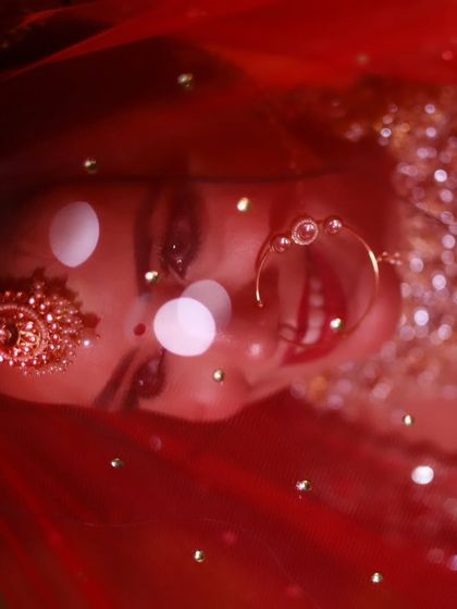 A creative shot through the bride's veil. The red tones and sparkling details of the makeup and outfit create a truly magical effect.