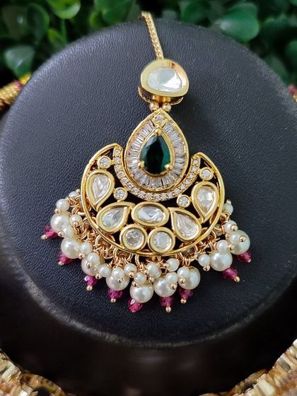This maang tikka features a pear-shaped green stone set in a kundan frame.