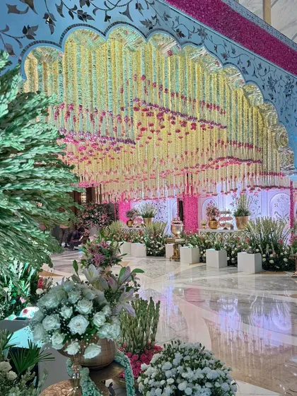 An enchanting entrance that sets the tone for the celebrations ahead. The floral-draped archway frames a view of the opulent hall, inviting guests into a world of magic. 🌿