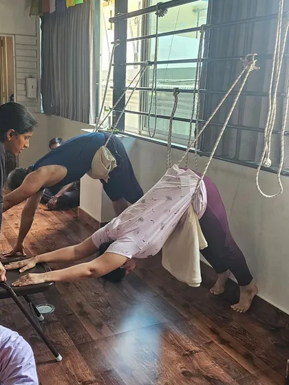 Students use wall ropes for a supported, restorative version of Downward-Facing Dog, allowing for deep release in the shoulders and back.