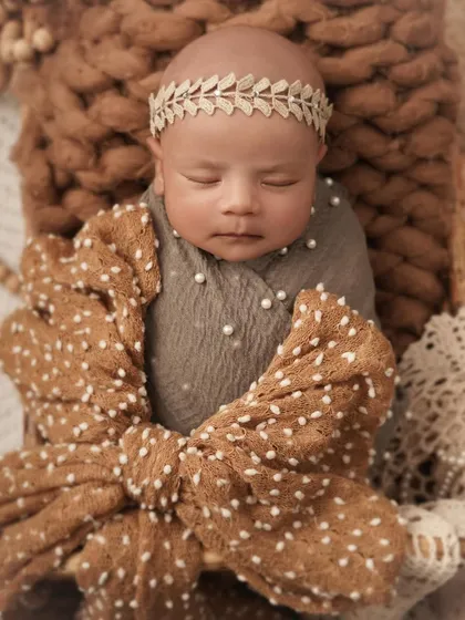 A sweet, sleeping portrait of a one-month-old baby, wrapped snugly with a large bow. The earthy tones and soft textures create a warm and comforting atmosphere.