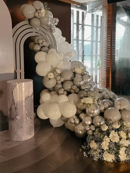 A close-up of the elegant monochrome balloon decor. The arrangement combines grey, white, and metallic silver balloons with sprigs of baby's breath for a soft, sophisticated look.
