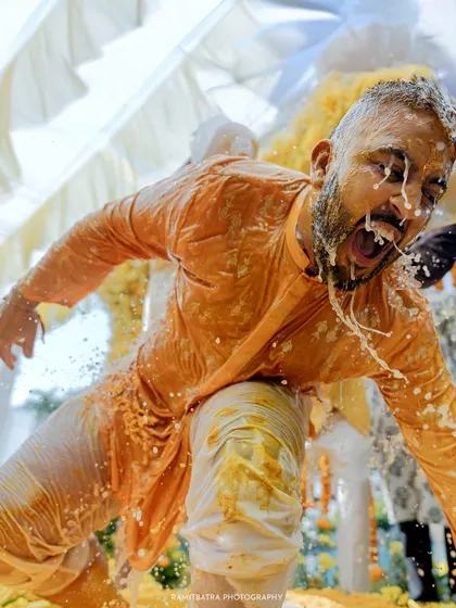 A dynamic, candid shot capturing the groom's reaction mid-splash during his Haldi ceremony. This is pure, unscripted fun.