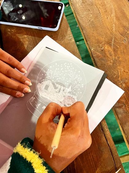 A participant at our Boho Bazaar workshop carefully tracing a winter scene onto parchment paper to create a delicate Christmas ornament.