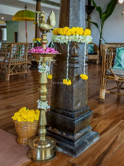 A traditional brass 'diya' (lamp) stands next to a stone pillar adorned with marigolds, embodying the sacred and beautiful spirit of a Haldi ceremony.