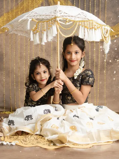Two sisters celebrating Onam, sharing a moment of affection under a traditional muthukuda. My festive sessions are designed to honor your family's traditions with authentic styling.