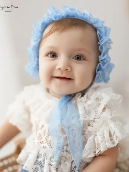 A stunning close-up of a baby girl with beautiful blue eyes, wearing a delicate lace bonnet. Her direct gaze is captivating.