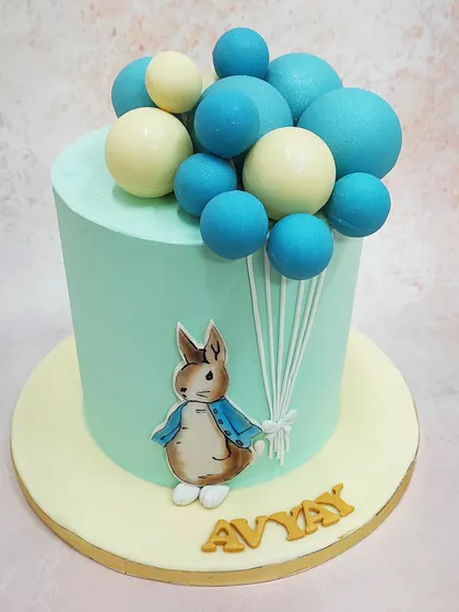 We bring a classic story to life with this Peter Rabbit cake, featuring the beloved character holding a bouquet of blue and white balloons.