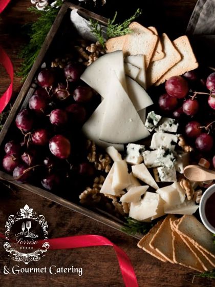 A festive, Christmas-themed charcuterie box. This arrangement features a variety of cheeses, including blue cheese, paired with grapes, nuts, and crackers, all nestled in a wooden box with a red ribbon.