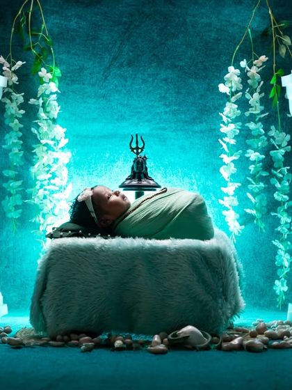 The same divine Maha Shivratri scene, captured with dramatic, low-key lighting. The ethereal blue glow highlights the sleeping baby and the sacred props, adding a layer of mystery and magic.
