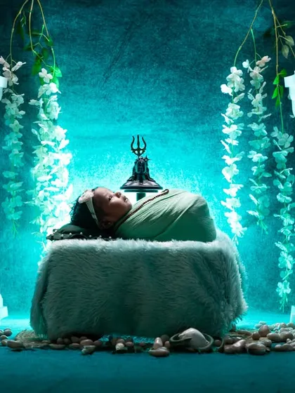 The same divine Maha Shivratri scene, captured with dramatic, low-key lighting. The ethereal blue glow highlights the sleeping baby and the sacred props, adding a layer of mystery and magic.
