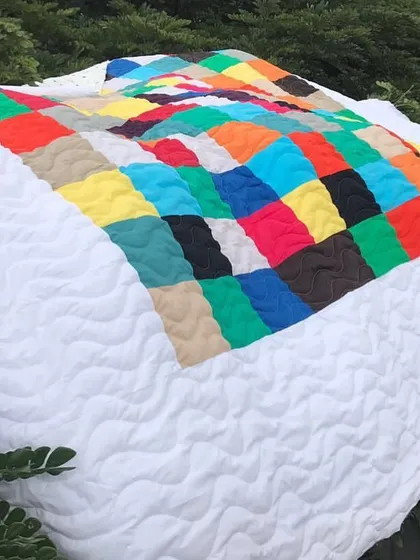 A colorful patchwork quilt with a white border, draped over bushes.