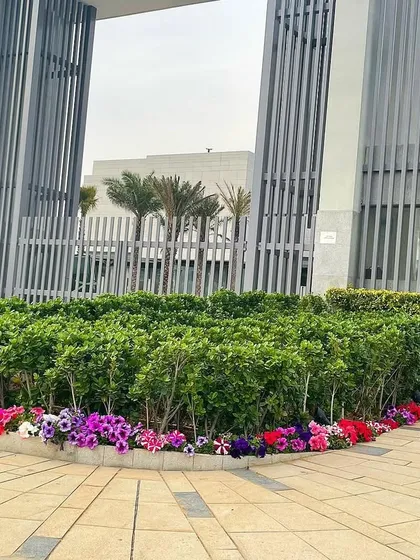 The entrance to a Faridabad property, featuring a large central planter filled with dense green hedges and a colorful border of seasonal petunia flowers. This creates a grand and welcoming first impression.