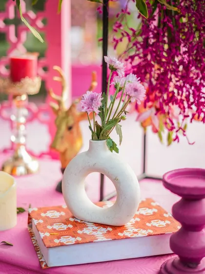 A close-up detail shot from a pink-themed Mehendi. The modern donut vase, colourful book, and hanging orchids create a chic and stylish vignette.