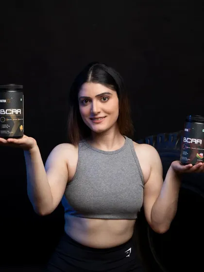 This shot is designed to showcase product variety. The model presents two different BCAA supplement containers, an effective technique for demonstrating a range of flavors or formulas in a single, clean image for an e-commerce catalog.