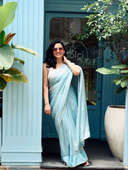 A poised and elegant photo in the same blue saree, taken in front of a picturesque cafe. This shot has a high-fashion, editorial feel, demonstrating my ability to create stunning visual content.