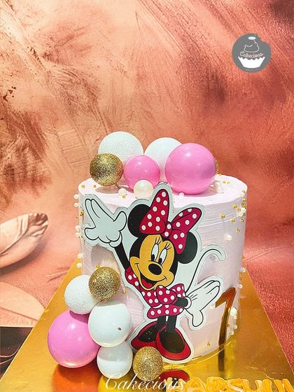 A sprinkle of Minnie Mouse magic for a first birthday. This pretty pink cake features a Minnie cutout, decorated with pink, white, and gold spheres for a touch of sparkle.