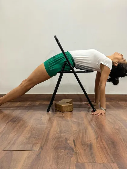 Here, a chair and blocks are used to practice Purvottanasana. The blocks under the hands elevate them, reducing wrist strain, while the chair supports the hips, making the pose more accessible.