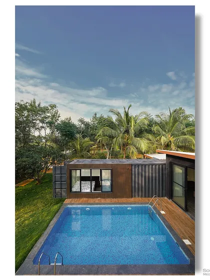 An aerial view of the container home and its private pool. This perspective showcases the project's layout and the beautiful contrast between the dark structure, the blue water, and the green landscape.