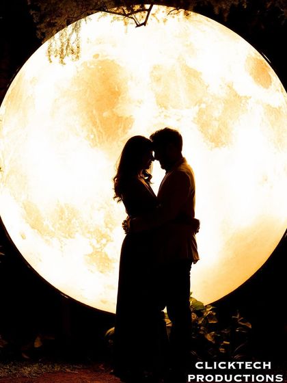 A classic silhouette of a couple embracing in front of a large, warm-toned moon prop, creating an iconic and romantic image.
