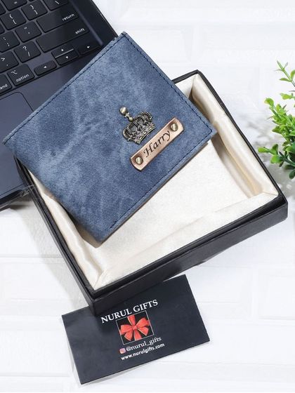This personalized blue denim wallet with a crown charm is displayed on a desk, showing it as a stylish accessory for everyday use.