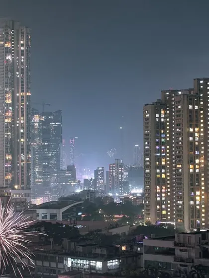 A long-exposure shot of Diwali fireworks exploding over the Mumbai cityscape, lighting up the night sky between illuminated residential towers.