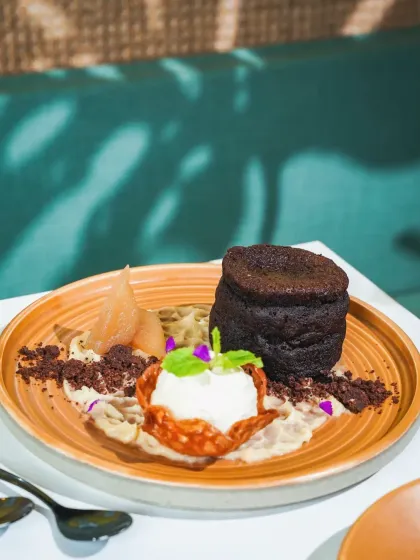 A decadent chocolate lava cake with vanilla ice cream and pear compote. The play of light and shadow on the cafe's teal green sofa adds a touch of ambiance to this dessert shot.