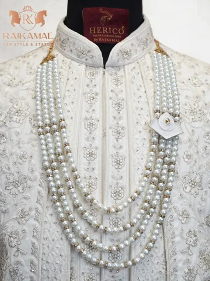A close-up of a white sherwani adorned with a five-layered pearl mala, an essential accessory for a majestic groom's outfit.