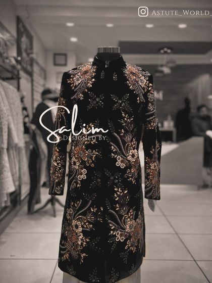 A black sherwani on a mannequin, covered in a dense floral embroidery pattern. The detail and coverage of the embroidery make it a truly luxurious piece.