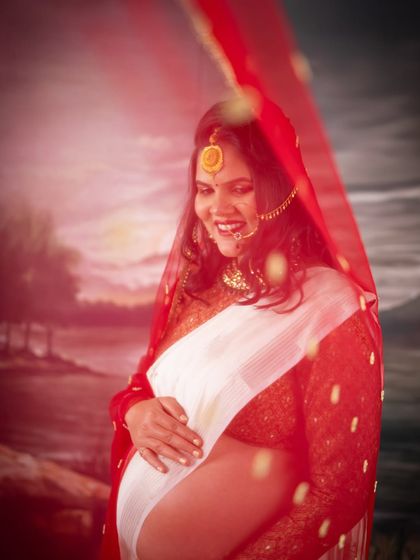 An artistic shot of a mom-to-be in a white and red traditional saree. The sheer red veil adds a layer of mystique and beauty to this culturally rich portrait.
