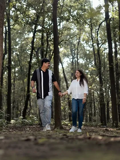 A candid shot of a couple walking hand-in-hand through a beautiful forest path. This captures a simple, happy moment in a serene natural environment.