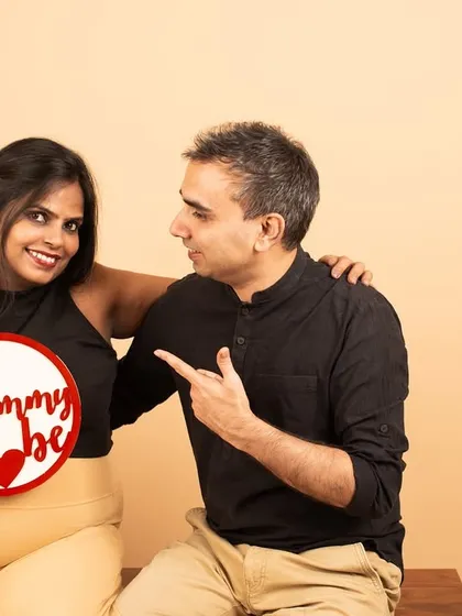 It's her turn. The couple playfully switches roles with the 'Mommy to be' sign, adding a touch of humor and personality to their studio session.