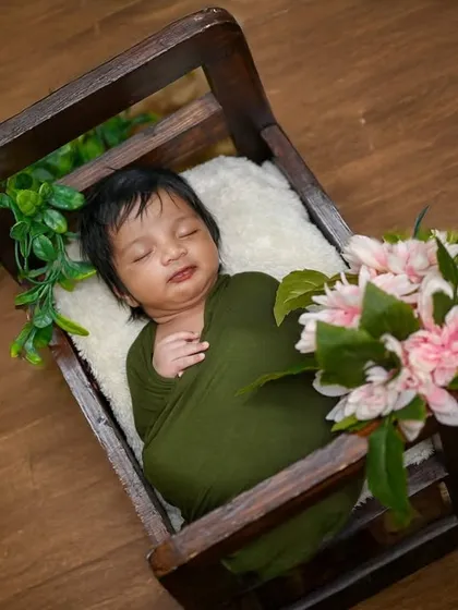 A simple, classic pose of a newborn wrapped in olive green, resting in a wooden crate. The focus is all on the baby's peaceful state.