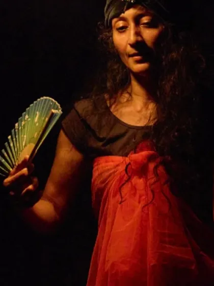 A contemplative moment from a solo performance. The use of a simple prop like a fan and dramatic lighting helps create a specific mood and character.