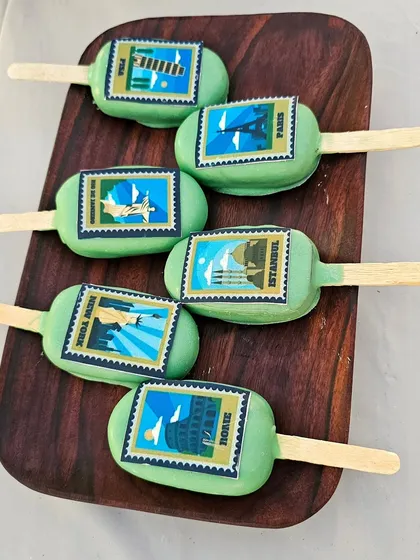 Cakesicles decorated to look like travel stamps from different cities like Paris, Rome, and New York.